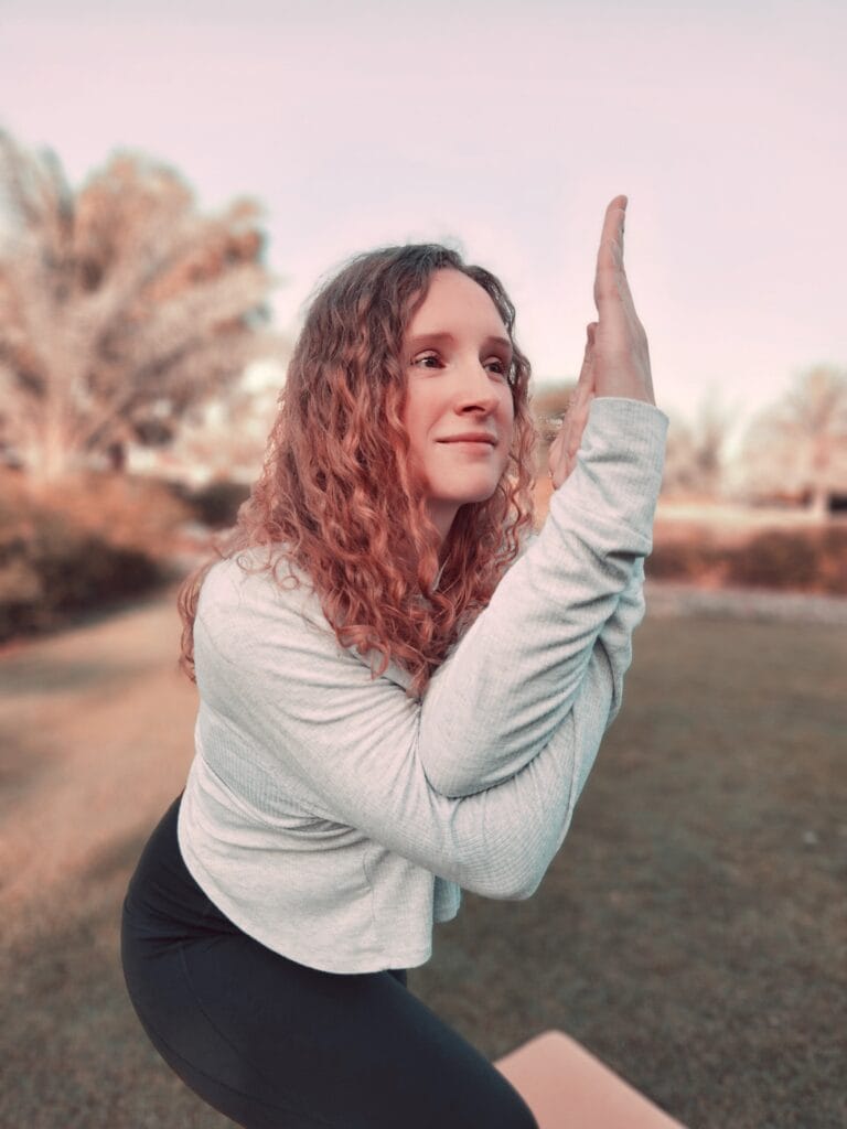 Alina Saibel in Eagle Pose (Garudasana) during an outdoor yoga session – balancing on one leg, other leg wrapped around the standing leg, arms entwined in front of the chest, body grounded and focused, a powerful expression of balance, strength, and focus in nature