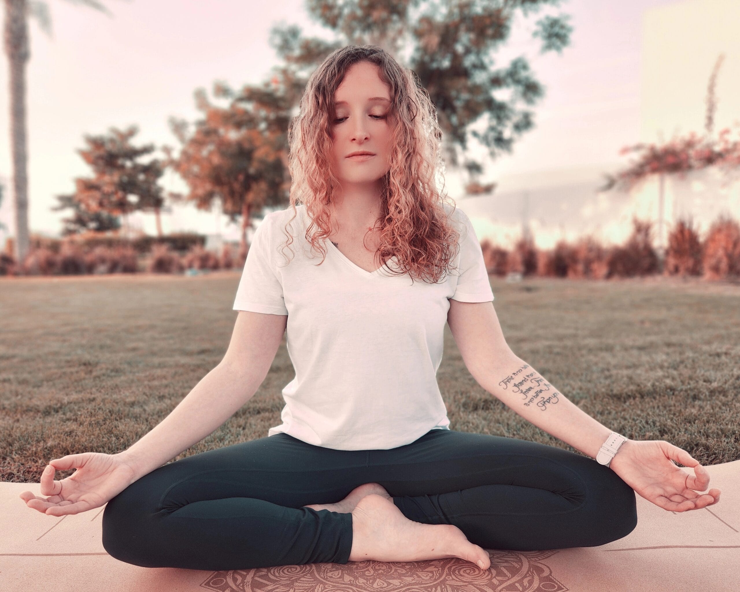 Alina Saibel seated in Easy Pose (Sukhasana) during an outdoor yoga session – legs crossed, spine tall, hands resting on the knees, palms open, eyes closed, radiating calm, balance, and peaceful presence in nature