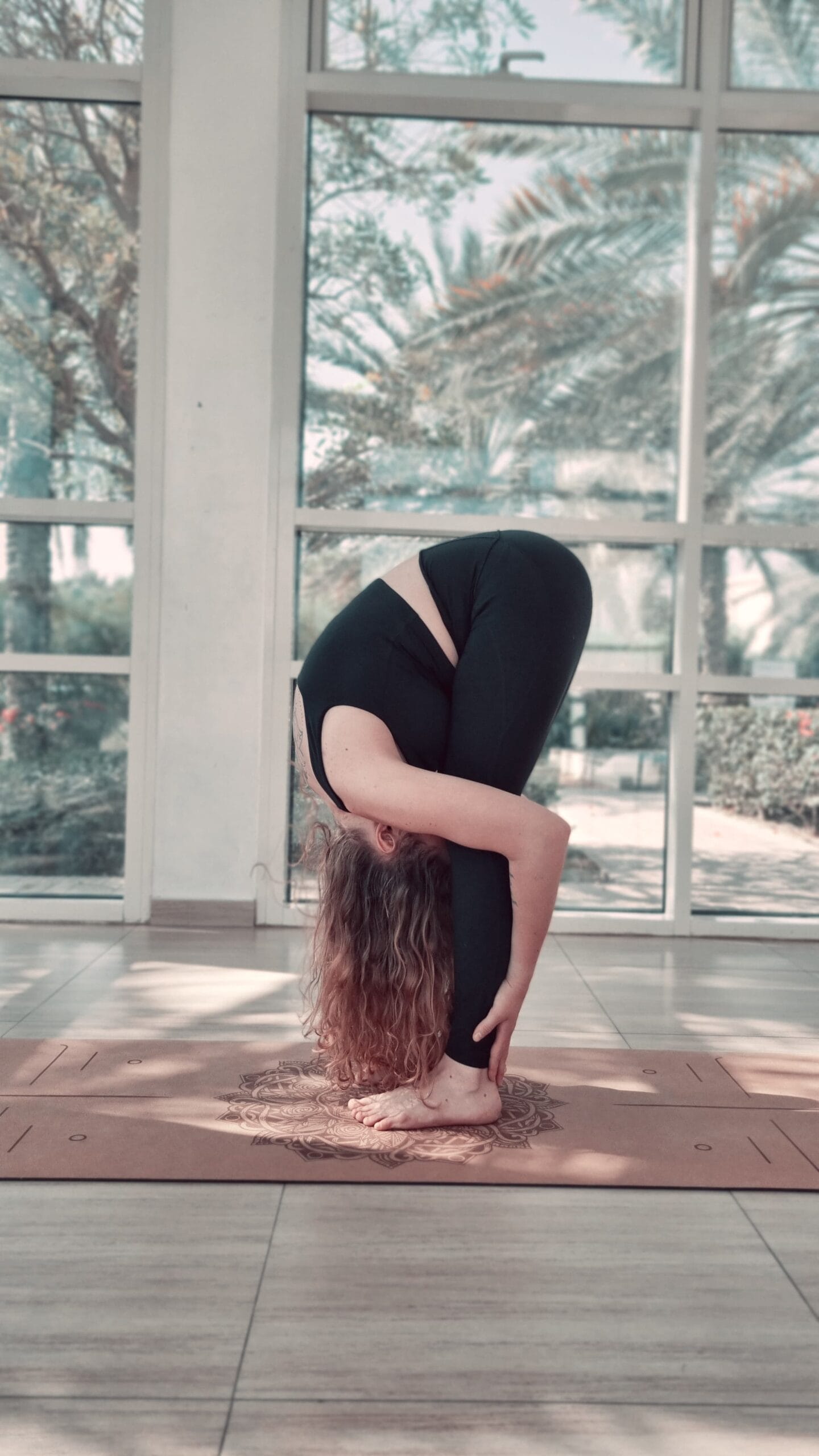 Alina Saibel in Standing Forward Fold (Uttanasana) during an outdoor yoga session – legs straight, torso folded over the legs, head relaxed, arms reaching down towards the earth, a moment of surrender and release in nature
