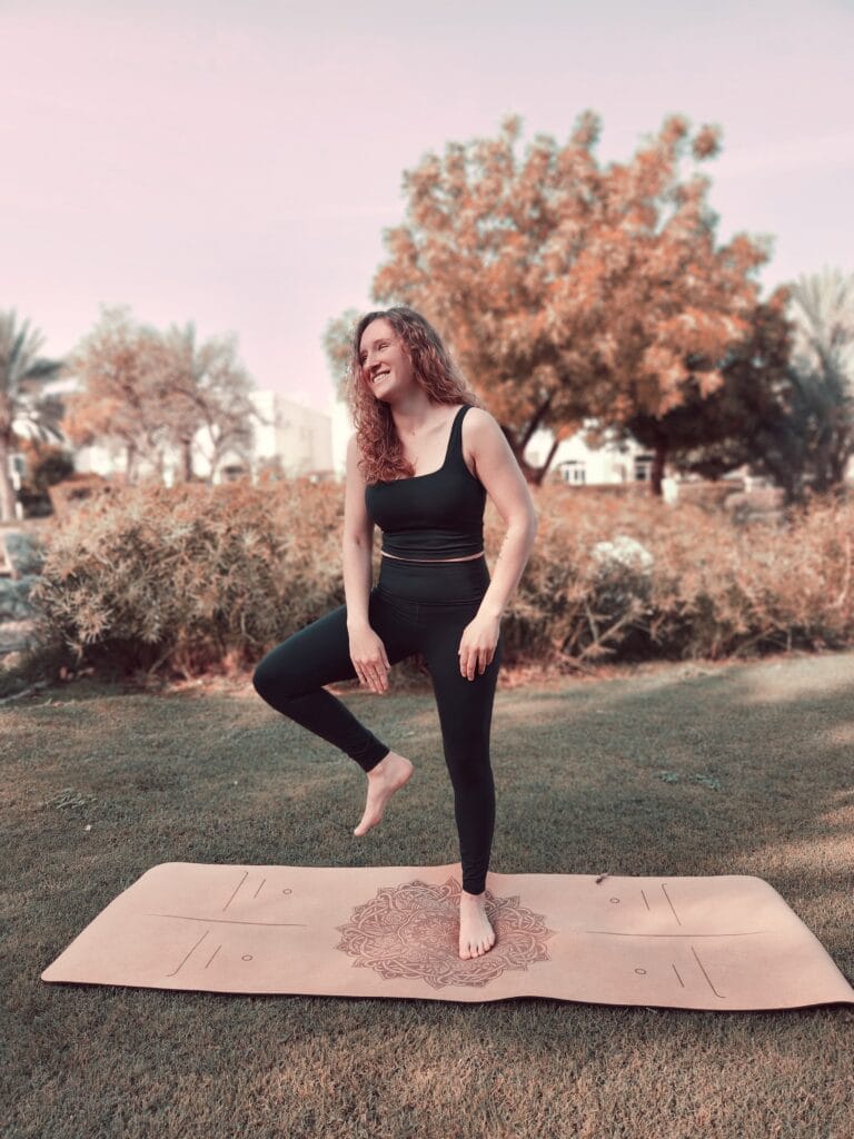 Alina Saibel, yoga instructor, laughing while playfully falling out of Tree Pose (Vrikshasana) – a lighthearted moment from a yoga class, showing the real journey of practice