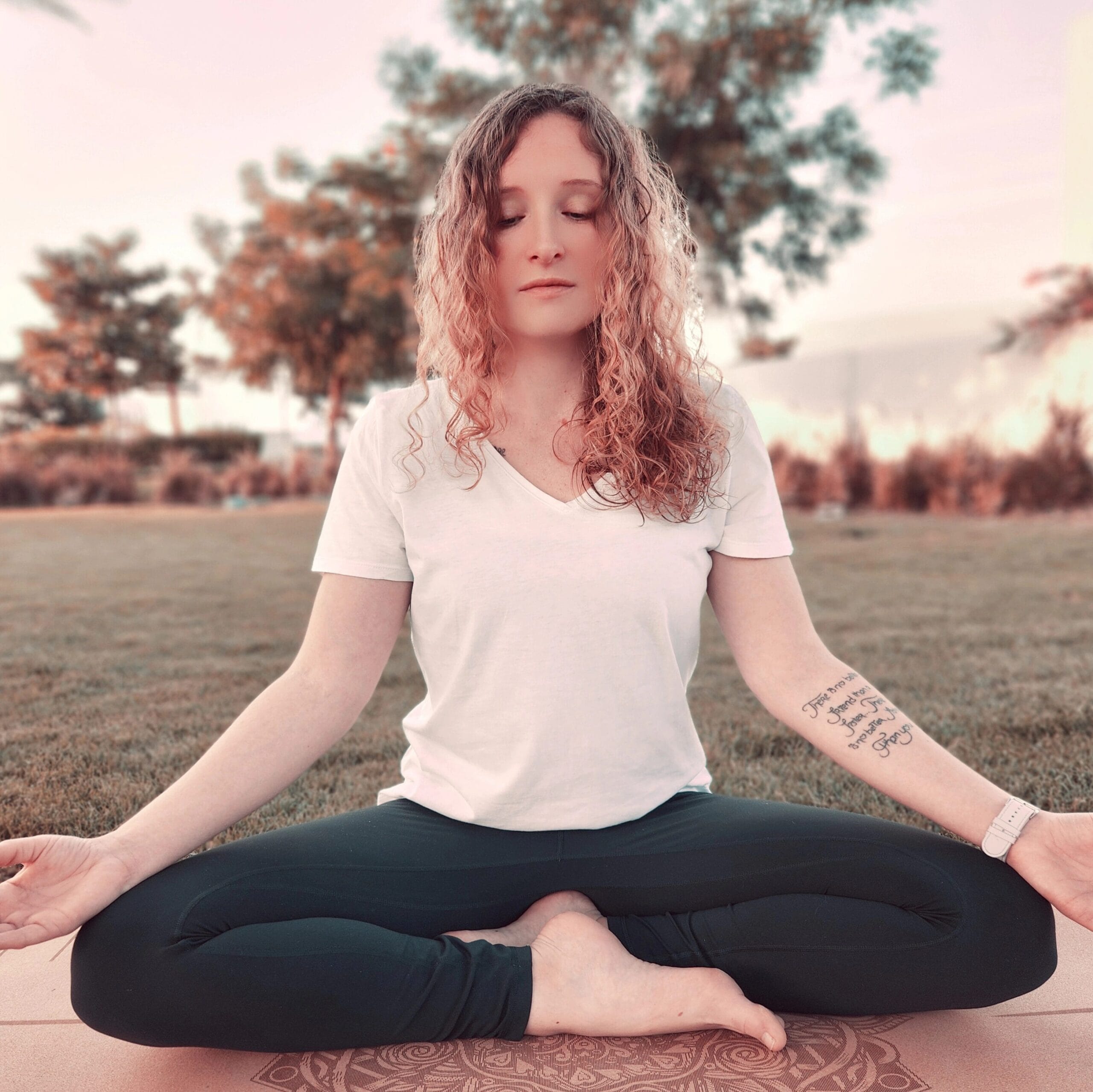 Alina Saibel seated in Easy Pose (Sukhasana) during an outdoor yoga session – legs crossed, spine tall, hands resting on the knees, palms open, eyes closed, radiating calm, balance, and peaceful presence in nature